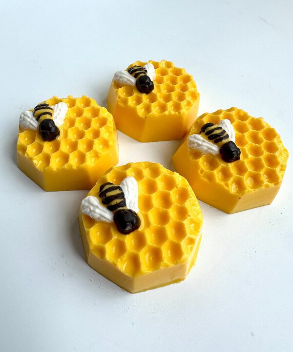 Four hexagonal yellow honeycomb-themed chocolates with bee decorations rest on a white surface.
