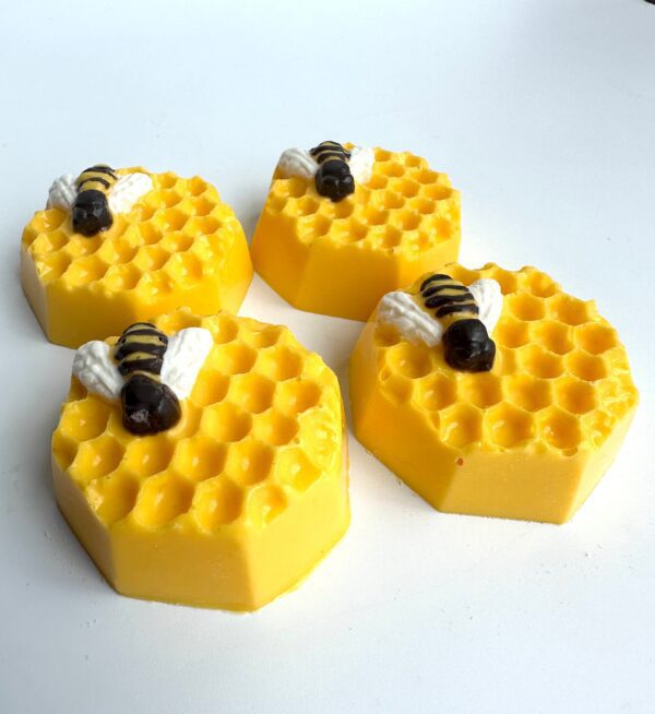 Four yellow hexagonal treats, each featuring a decorative bee on top, mimicking honeycomb patterns, are displayed on a white surface.