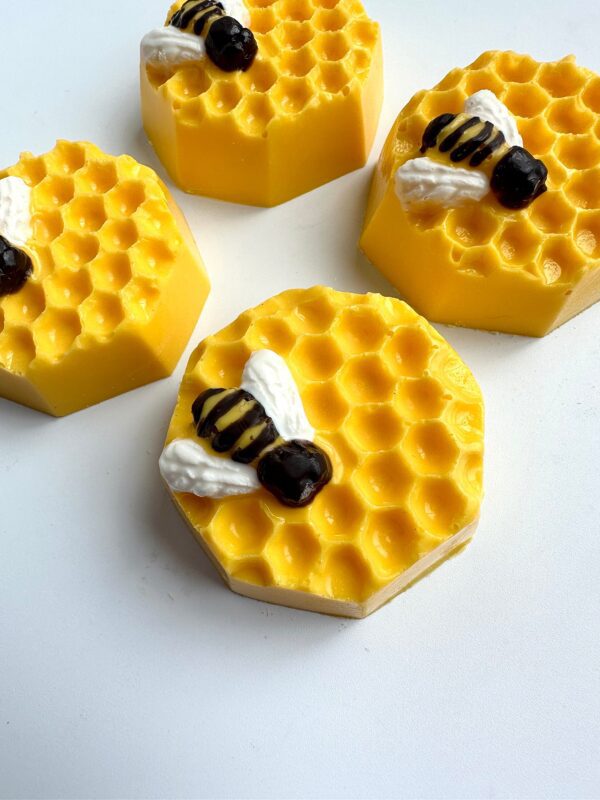 Four hexagonal chocolate-covered Oreos resembling honeycomb, topped with decorative bees, set on a white background.