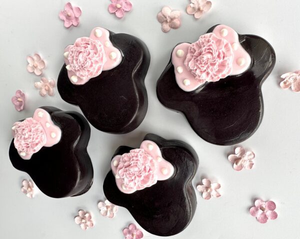 Four 12-Minnie chocolate covered Oreos in black bear shapes with pink flower decorations and small scattered pink flowers on a white background, perfect for party favors, birthday parties, or baby showers.