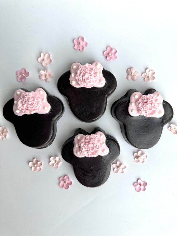 Four Minnie-themed Oreos shaped like black bear paws with pink floral decorations, surrounded by small pink flowers on a white background, from the "12-Minnie Chocolate Covered Oreos For Party Favors/Birthday Party/Baby Shower" set.