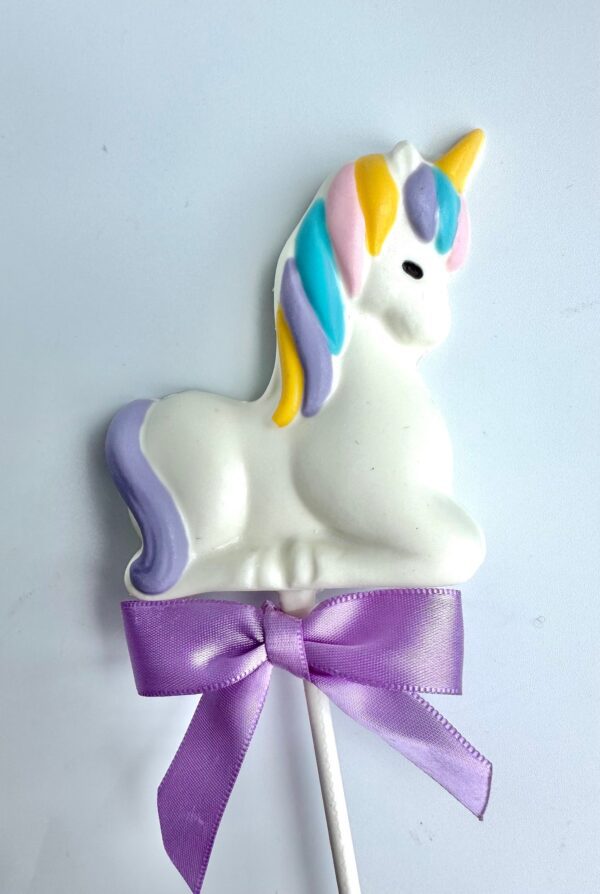 White chocolate unicorn lollipop featuring a white body, multicolored mane, and a purple bow on the stick, ideal for baby showers or birthday parties.