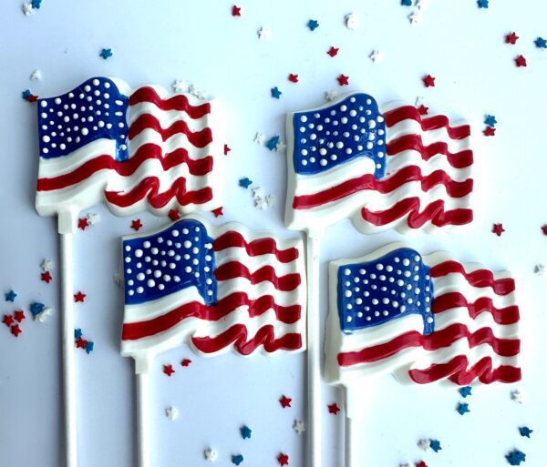Five lollipops shaped like the American flag, part of the 12 White Chocolate American Flag Lollipops set for Memorial Day or July 4th, are surrounded by star-shaped sprinkles on a white background.