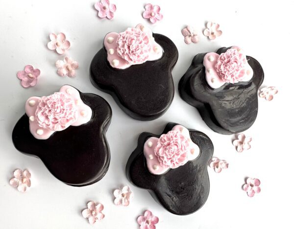 Four Minnie-themed chocolate-covered Oreos designed as black paw shapes with pink floral decorations, adorned with small pink flowers on a white background.