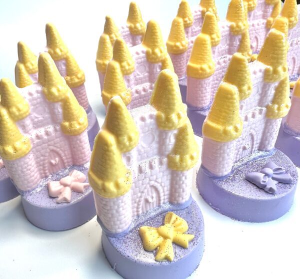 Rows of pastel pink and yellow castle-shaped soap bars with lavender bases and small decorative bows resemble the 12 Fairytale Castles on Chocolate Covered Oreos, ideal for princess, rainbow, or unicorn parties.