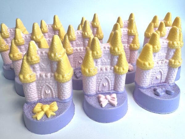 A collection of soap bars, resembling pink castles with yellow towers and bows, is elegantly arranged on a light background.