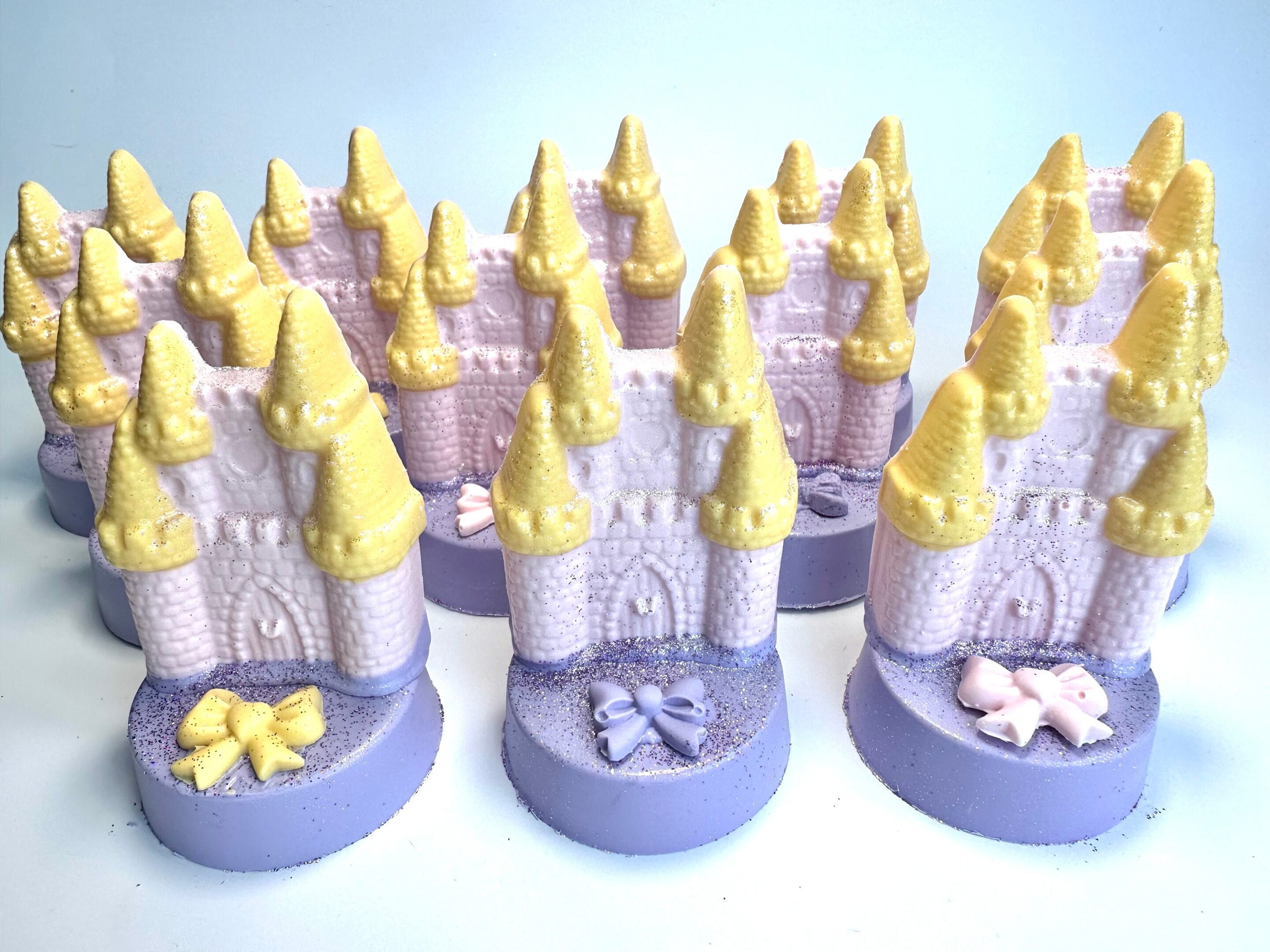 Pastel-colored, castle-shaped soap bars with yellow roofs and decorative bows sit atop chocolate-covered Oreos in a set of 12, ideal for princess, rainbow, or unicorn parties.