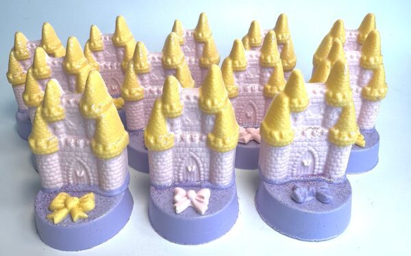 12 pink and purple castle-shaped soaps with yellow towers are set on chocolate-covered Oreo bases, each adorned with decorative bows.