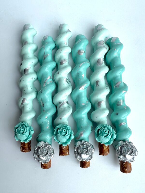 Six Tiffany Blue and silver chocolate-covered caramel pretzel sticks with metallic accents and decorative flowers are displayed on a white surface.