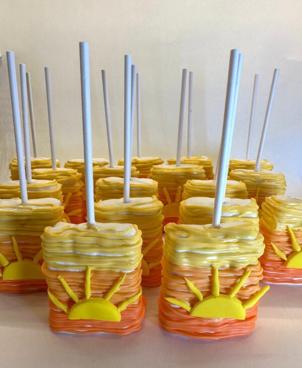 Sunset Ombré chocolate-covered Rice Krispie treats with sun decorations and white sticks, arranged in rows.