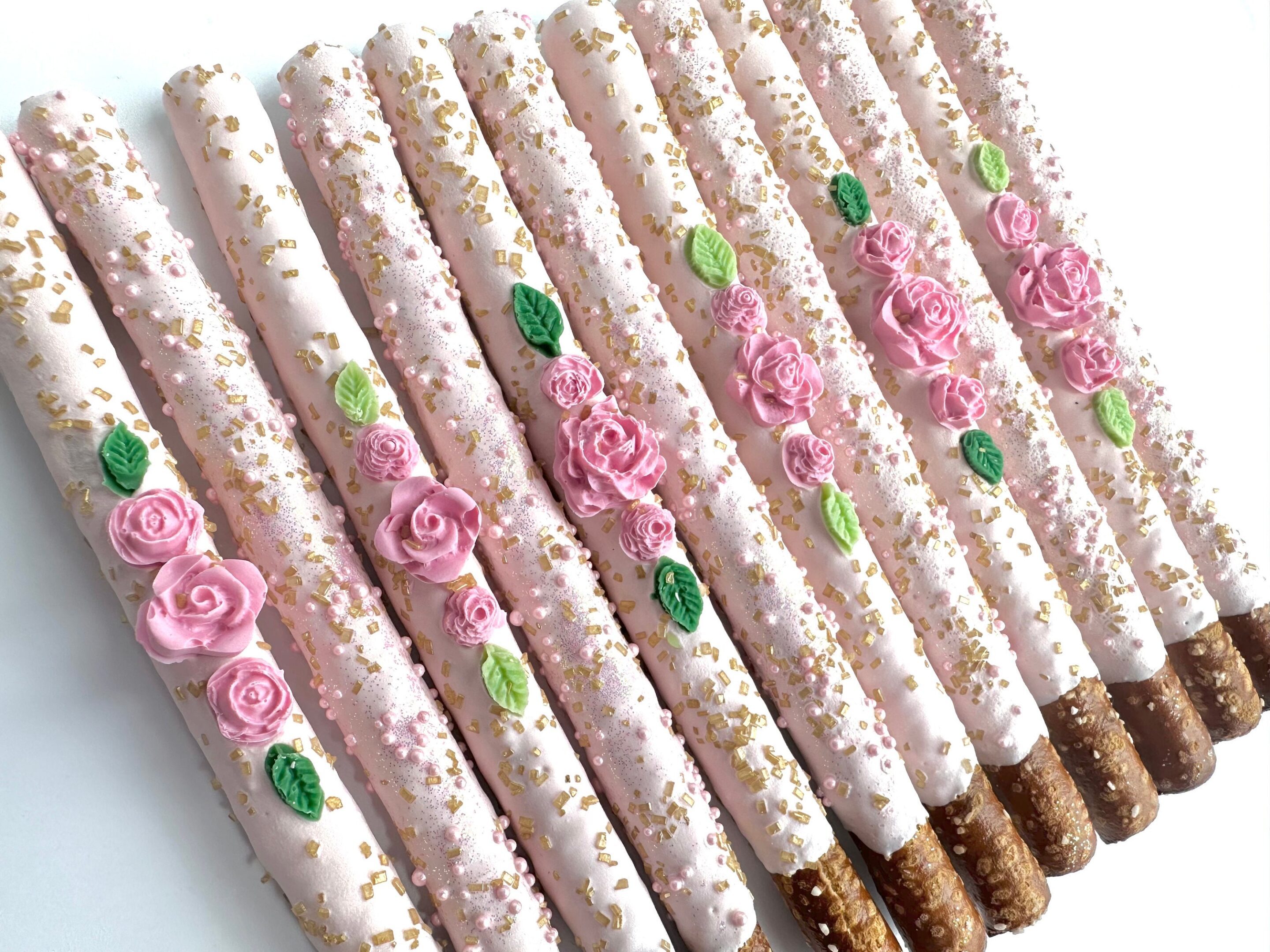 Delight in our 12-pale pink chocolate pretzels, ideal for parties or favors. Elegantly decorated with pink icing, accented by pink roses, green leaves, and a sprinkle of gold and pink sugar.