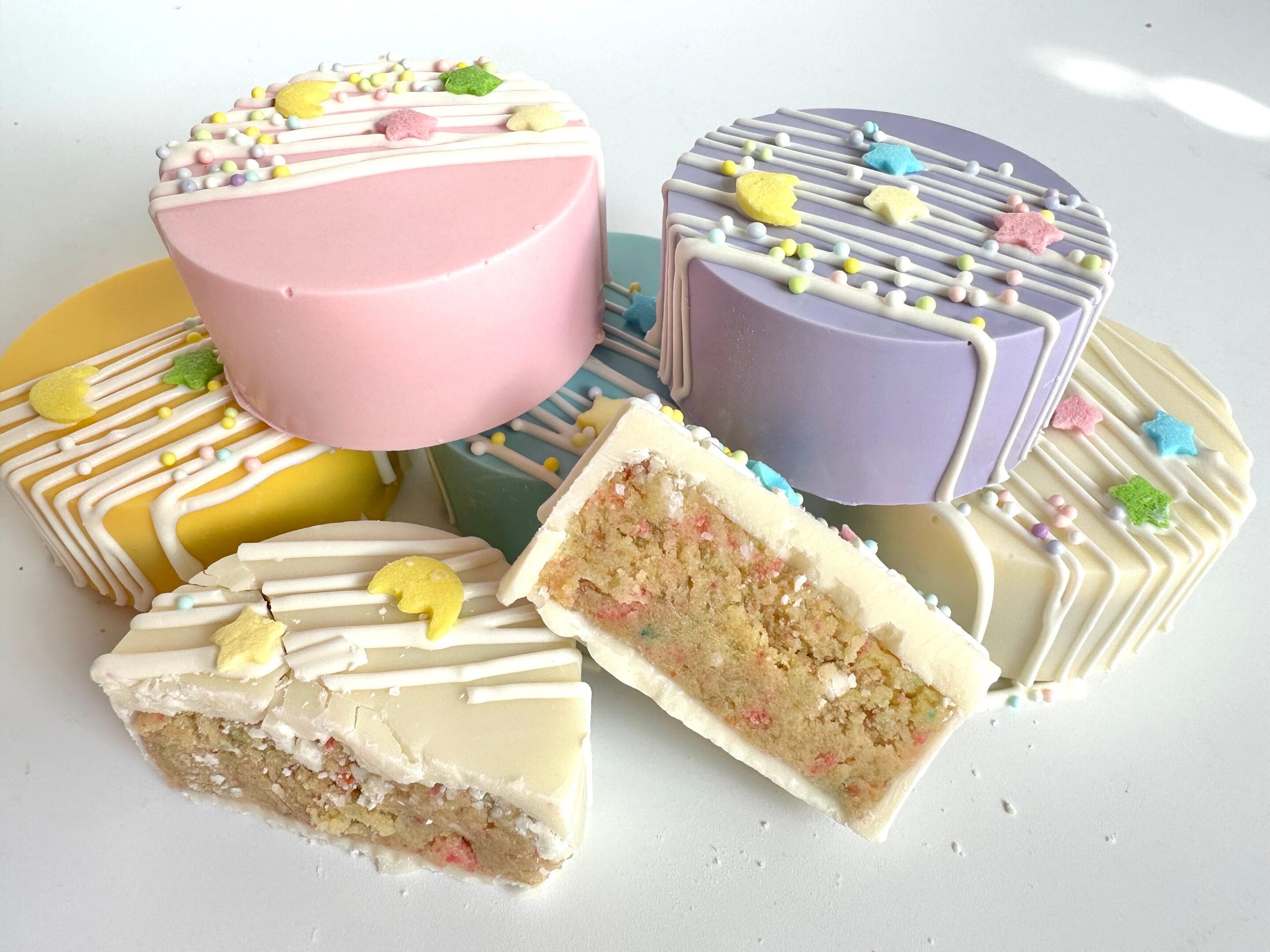 12-Moon & Stars White Chocolate Cake Pucks, featuring icing lines and star-shaped decorations, are showcased as vibrant slices on a white surface, perfect for birthday party favors or baby shower gifts.