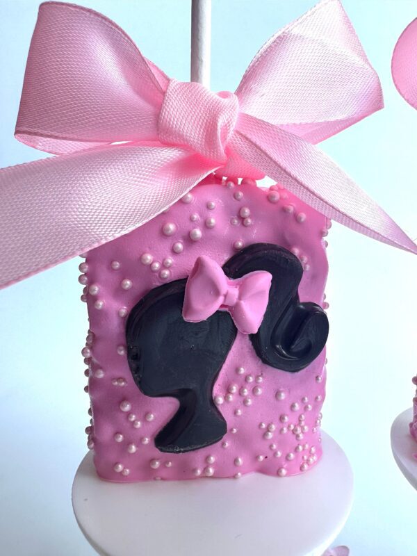 Pink chocolate-covered Rice Krispie Treat with a silhouette of a woman's head, a bow on pink icing, small pearls, and topped with a pink ribbon.