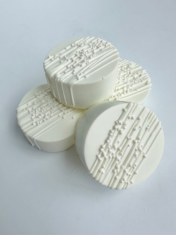 Four white chocolate-covered Oreos, featuring textured icing patterns, are arranged on a white surface.