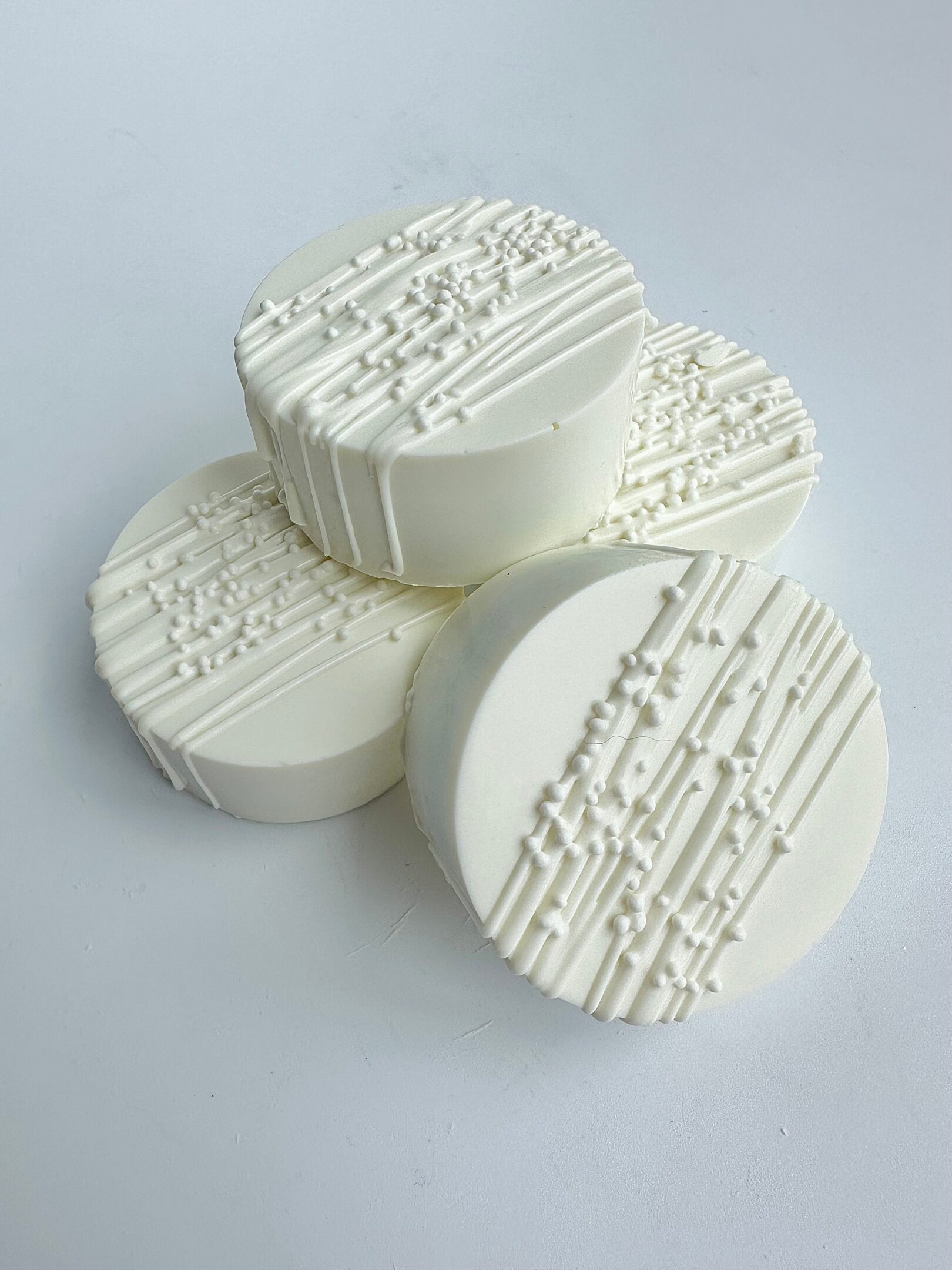 Four white chocolate-covered Oreos, featuring textured icing patterns, are arranged on a white surface.