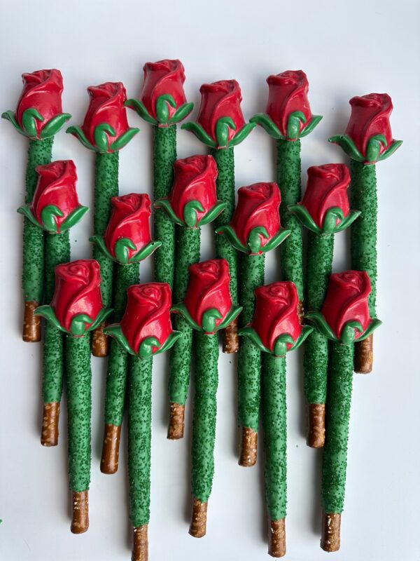 Seventeen chocolate-covered pretzel rods from the 24-LONG STEM ROSES collection, adorned with red roses and green leaves, are arranged on a white surface.