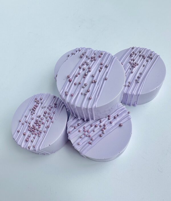 Four lavender chocolate-covered Oreos, topped with drizzled icing and small edible pearls.