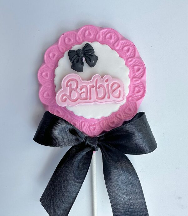 A Barbi Chocolate Lollipop featuring pink icing, a black bow, and "Barbie" in the center from the 12-Barbi Chocolate Lollipops for Birthday Party set.