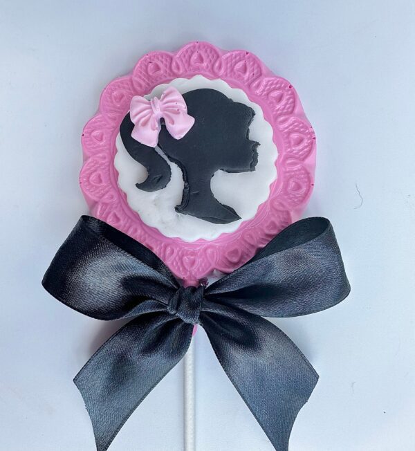 A Barbi Chocolate Lollipop featuring a black silhouette of a girl's profile with a pink border, adorned with a pink bow, and topped with a large black bow.