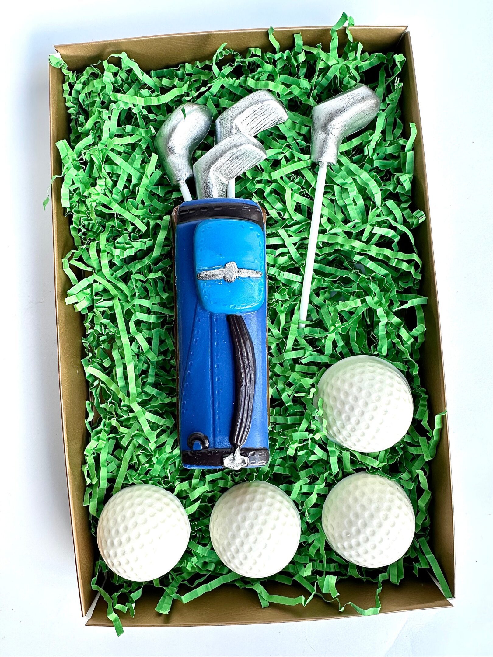 A green box contains a Golf Bag With Clubs & Golf Balls Chocolate Gift Set, featuring a blue golf bag and chocolates shaped like golf clubs and balls.