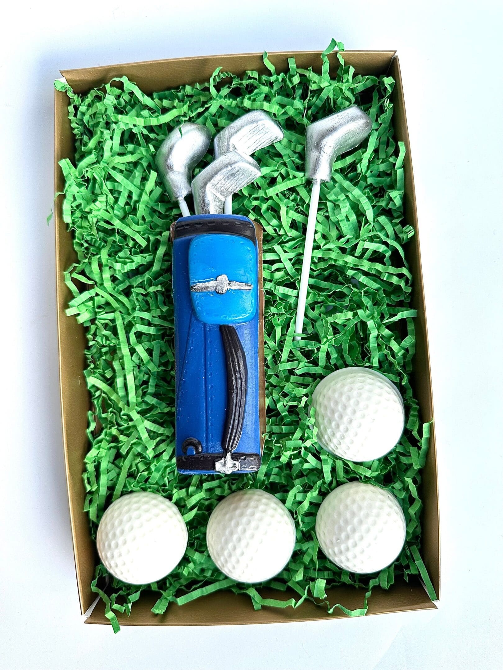 The Golf Bag With Clubs & Golf Balls Chocolate Gift Set includes a blue golf bag, three clubs, and four balls, arranged on green shredded paper in a box. Ideal for Dad's birthday or as a golf gift.