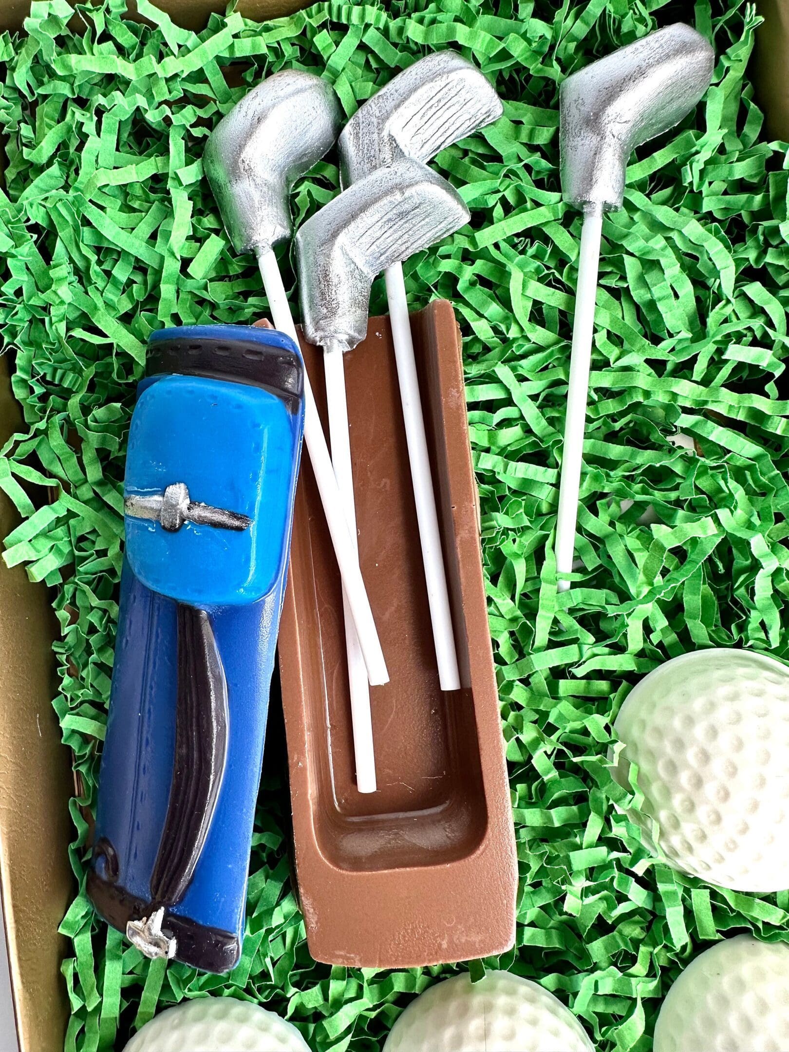 The Chocolate Golf Gift Set includes a blue golf-themed chocolate bag, club lollipops, and golf balls presented on green shredded paper, perfect for a dad or son birthday gift.