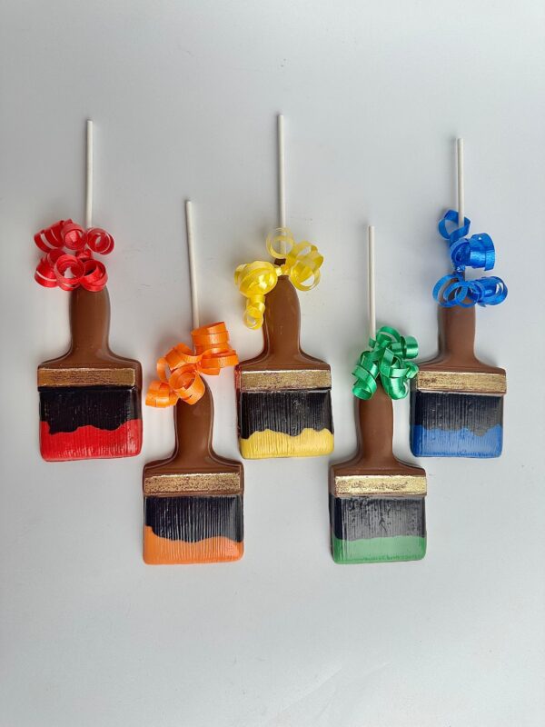 Five paintbrush-shaped chocolate lollipops with colorful ribbons, featuring red, orange, yellow, green, and blue colors on a white background from the set "12-Paint Brush Chocolate Lollipops For Birthday Party/Party Favors.