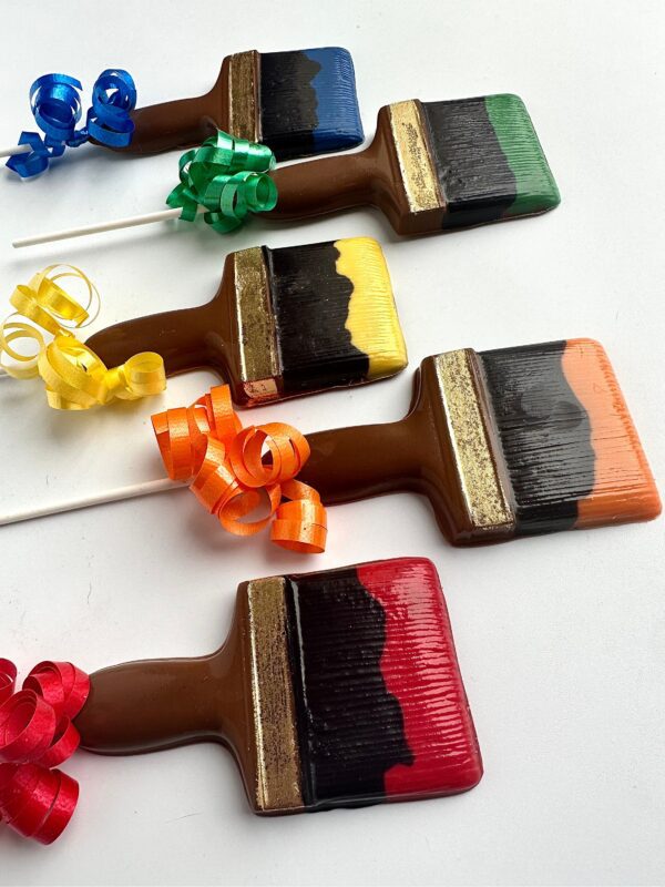 A set of 12 "Paint Brush Chocolate Lollipops For Birthday Party/Party Favors" with colored bristles and matching spiral ribbons are arranged on a white surface.
