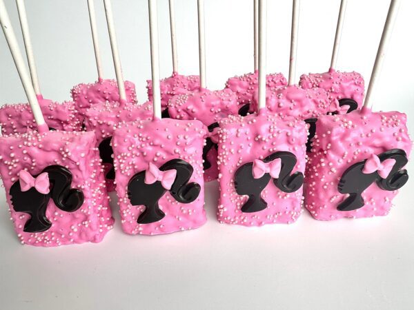 Barbi-themed Rice Krispie treats on sticks, coated in pink icing and white sprinkles, with a black silhouette and pink bow decoration.