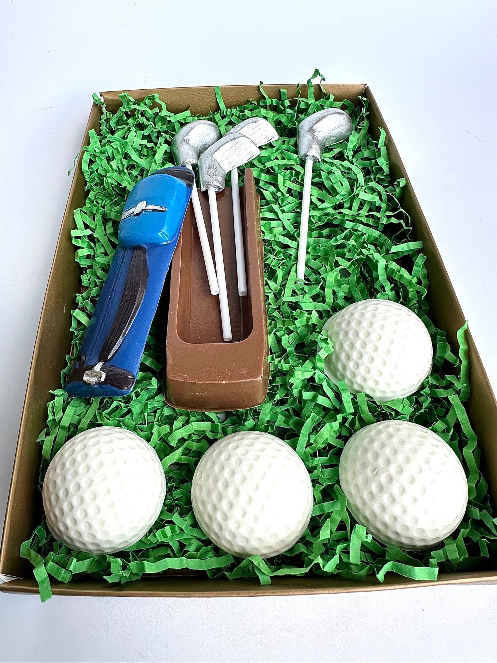 A Golf Bag With Clubs & Golf Balls Chocolate Gift Set, featuring chocolate shaped like golf balls, a blue golf bag, small silver club sticks, and brown chocolate wrapped in green paper strips. Perfect for Dad's Birthday or as a Son/Golf Gift.