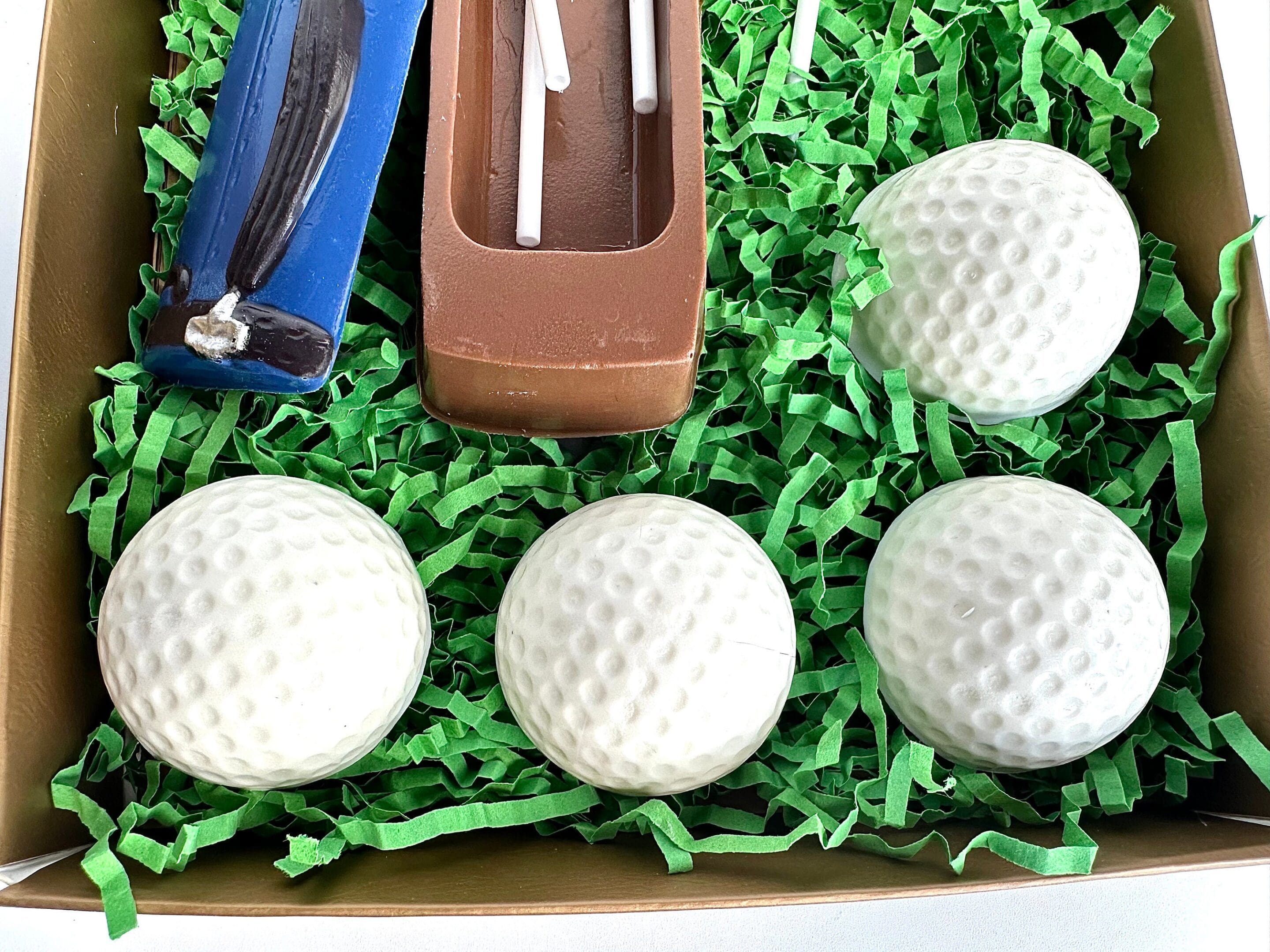 Gift set includes four golf ball-shaped chocolates and golf-themed tools, presented on green paper shreds.