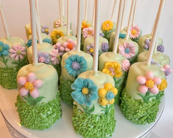 12-Flower Garden Themed Chocolate Covered Double Marshmallow Pops adorned with pastel flowers and green sprinkles on a platter.