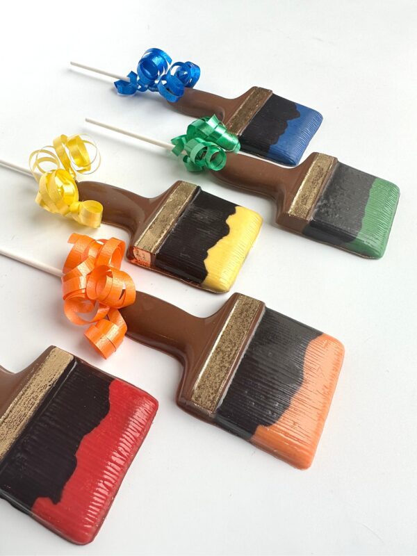 This set includes four paintbrush-shaped chocolate lollipops with red, orange, yellow, and blue striped colors, each adorned with matching curly ribbons.