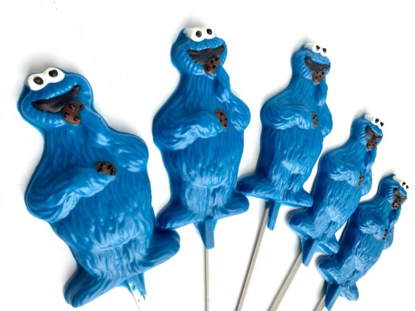 Five blue monster lollipop favors with googly eyes, each holding a brown cookie.