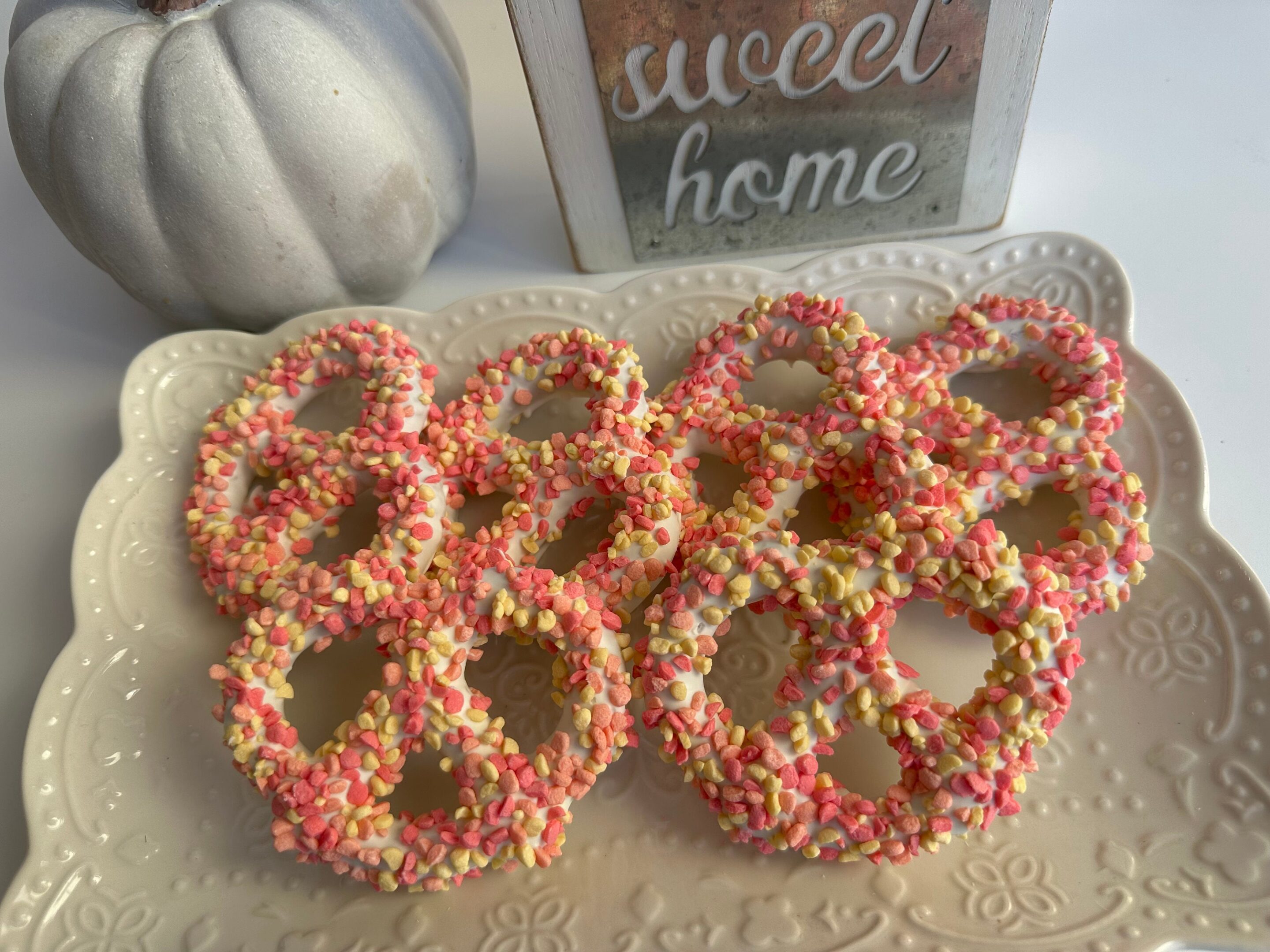 Strawberry shortcake pretzel twists are arranged on a decorative plate beside a small pumpkin and a "sweet home" sign.