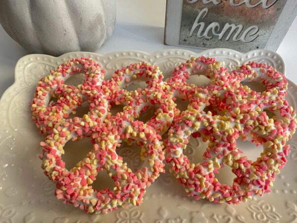 Strawberry Shortcake Pretzel Twists, white chocolate-covered with pink and yellow candies, elegantly arranged, perfect for birthday or baby shower gifts.