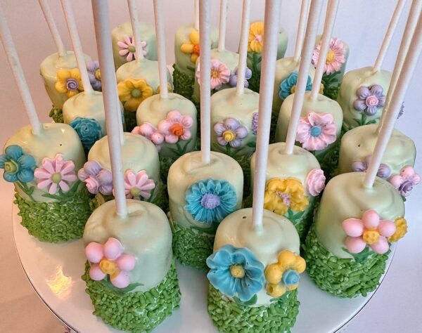 Twelve flower garden-themed green pops with floral decorations, displayed upright on a plate.