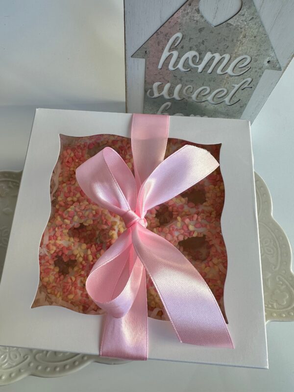 A decorated white box with a pink ribbon contains 12 strawberry shortcake pretzel twists and sprinkled cookies on a tray, with a "home sweet home" sign in the background.