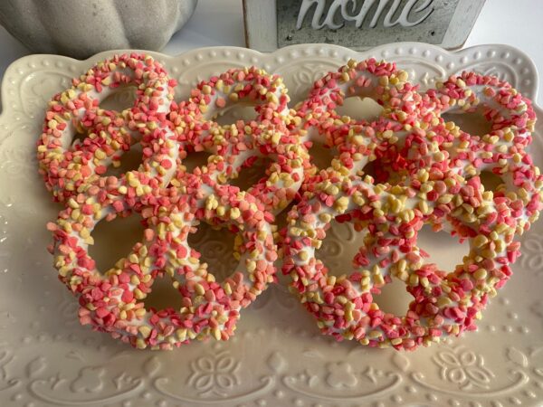 An assortment of pretzels with white chocolate coating, adorned with pink, yellow, and white candy bits, available in the 12-Strawberry Shortcake Pretzel Twist Gift Box for birthday or baby girl celebrations.