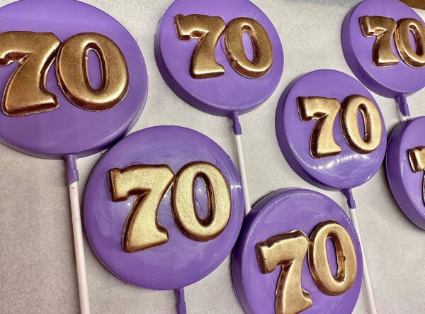 Purple lollipops with gold "70" decoration from the "12-Purple 70th Birthday/Anniversary Chocolate Lollipop/Party Favors/70th Birthday Party" set are laid on a white surface.