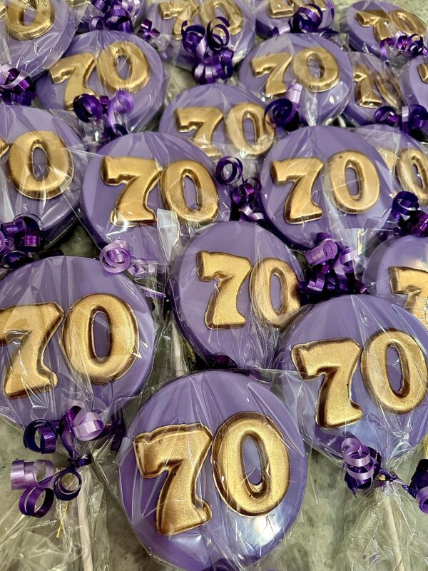 Celebrate with purple and gold '70' shaped cookies wrapped in clear plastic, adorned with purple ribbons, perfect as 12-pack chocolate lollipops or party favors for a 70th birthday or anniversary.