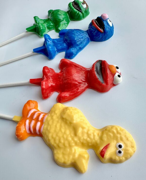 A lineup of 12 colorful assorted Sesame Character lollipops on sticks displayed against a white background, ideal as party favors for children's birthday celebrations.