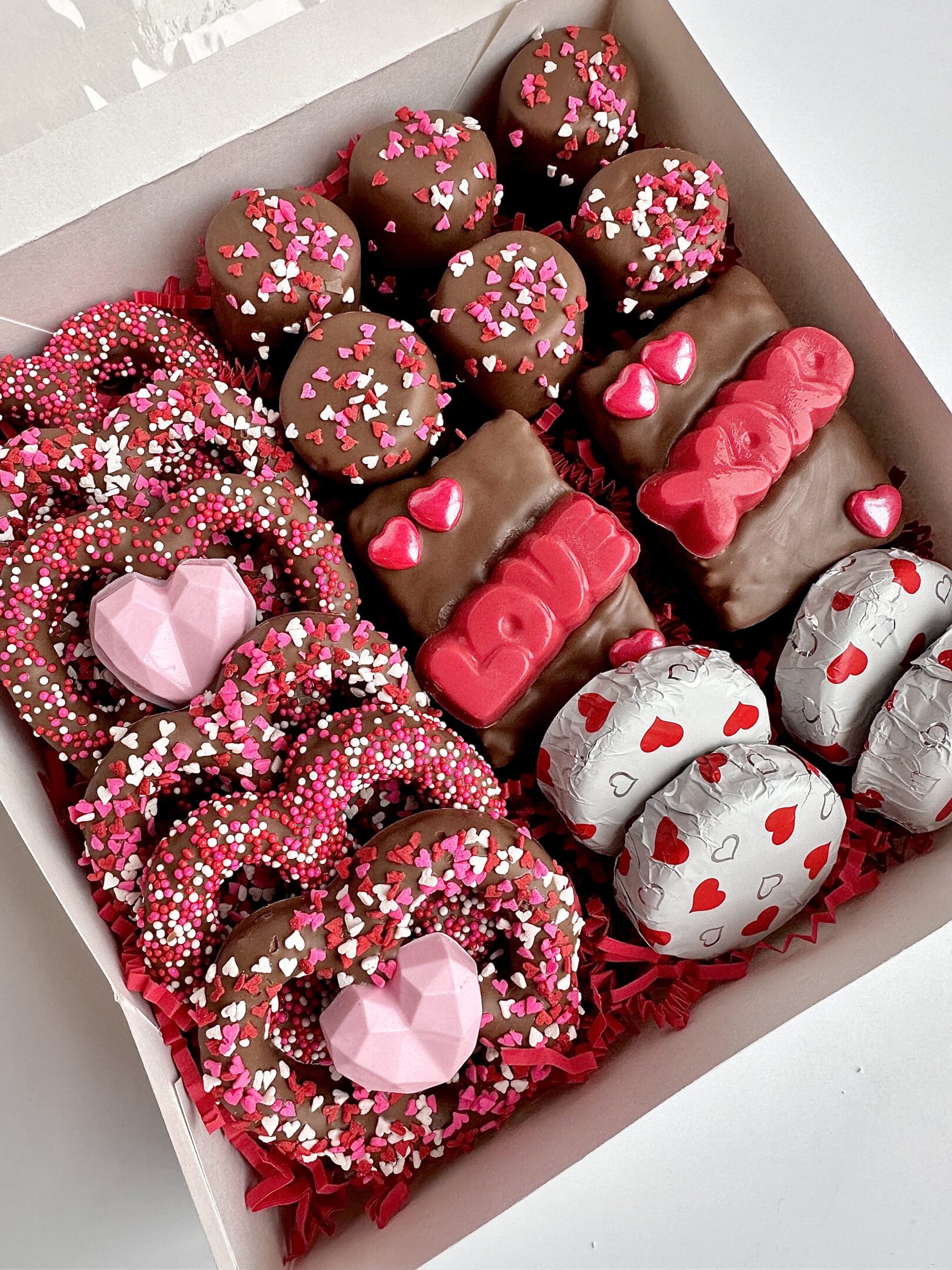A Milk Chocolate Treat Gift Box perfect for an anniversary, sweetheart, Valentine's Day, or birthday is adorned with pink and red heart-shaped sprinkles and candies.
