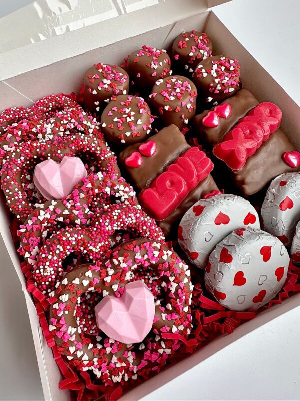 A Milk Chocolate Treat Gift Box, perfect for Valentine's Day, features pink and red hearts with heart-shaped, round, and rectangular chocolates.