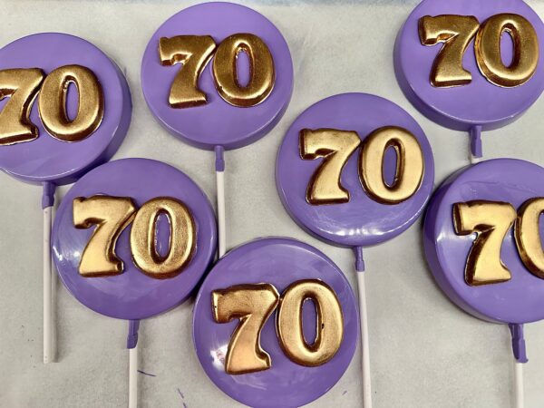 Purple lollipops with golden "70" numbers, part of the 12-Purple 70th Birthday/Anniversary Chocolate Lollipop collection, displayed on a white surface.