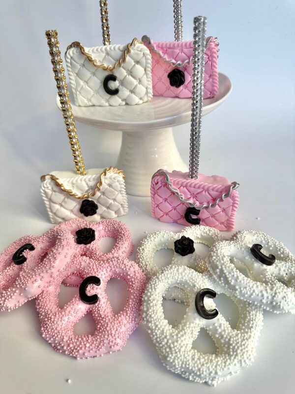 Quilted handbag cake pops with white and pink colors on a stand, surrounded by pretzels with pink and white sprinkles featuring decorative black "C" accents. Available as 12-Designer LOGO Purses for parties like birthdays or weddings.
