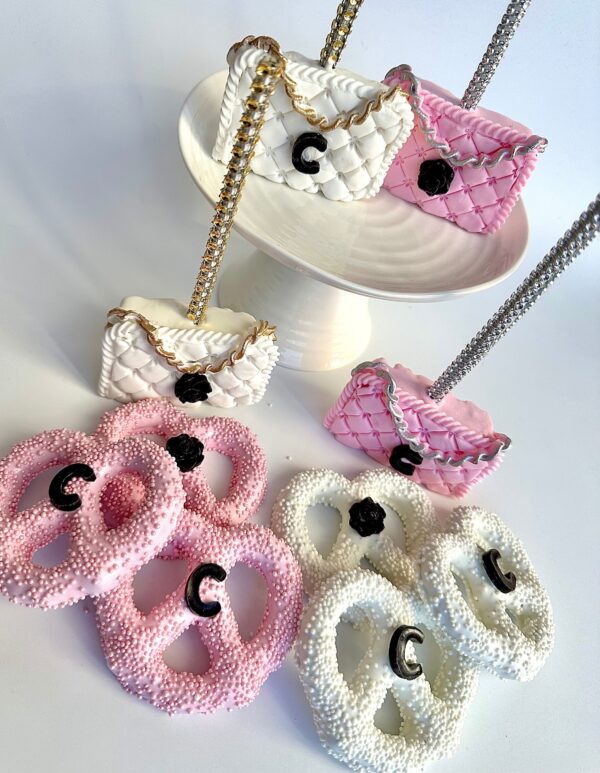 Chanel-inspired purse-shaped cookies in pink and white, placed on a pedestal, perfect as party favors for birthdays, weddings, or baby showers.