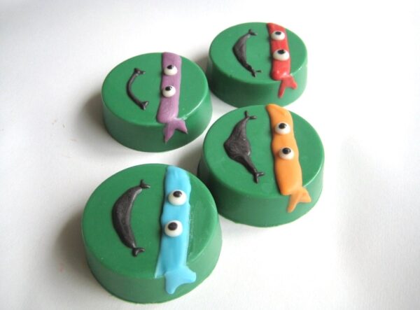 Four green chocolate-covered Oreos from the 12-Ninja Green Turtles set, featuring colorful narwhal decorations.