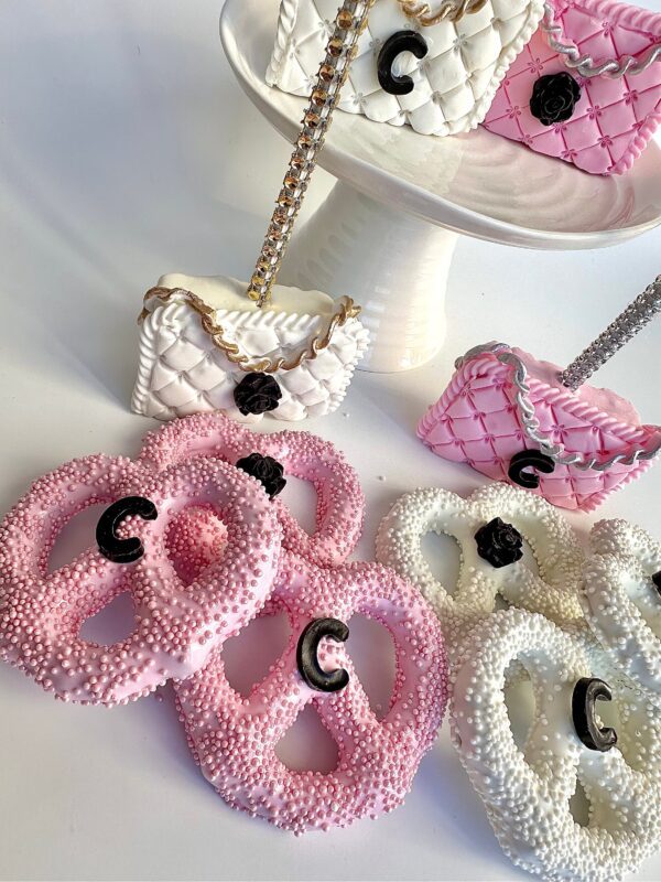Pink and white pretzels with black "C" letters are showcased alongside quilted purse decorations from "12-Designer LOGO Purses For Birthday Party/Wedding/Baby Shower/Party Favors/Purse Party" on a stand and table.