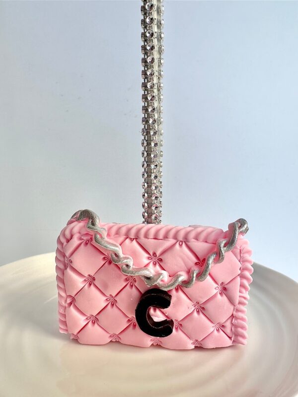 The 12-Designer LOGO Purses cake, featuring a pink quilted design with a silver chain and black "C" embellishment, is elegantly displayed on a white plate.